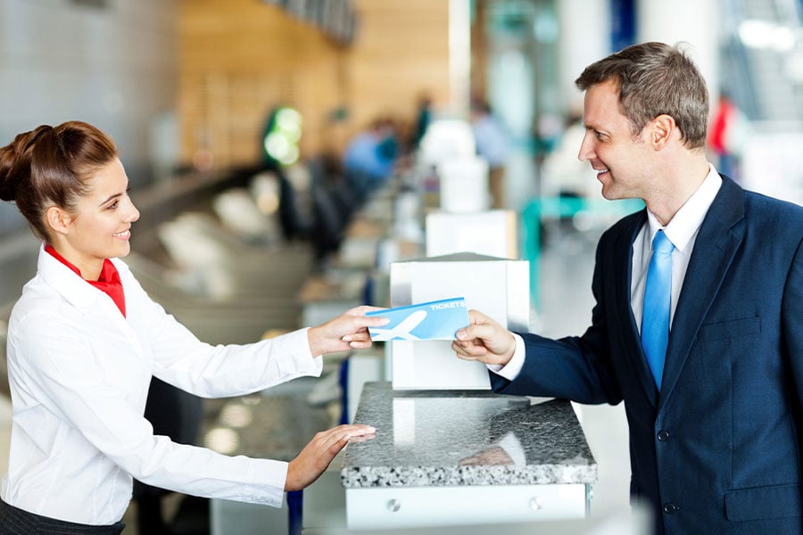 Airport agent in uniform hands boarding pass to businessman in suit at check-in counter.