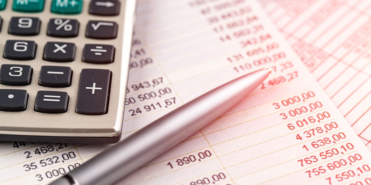 Calculator and pen rest on financial documents showing numerical data and calculations.