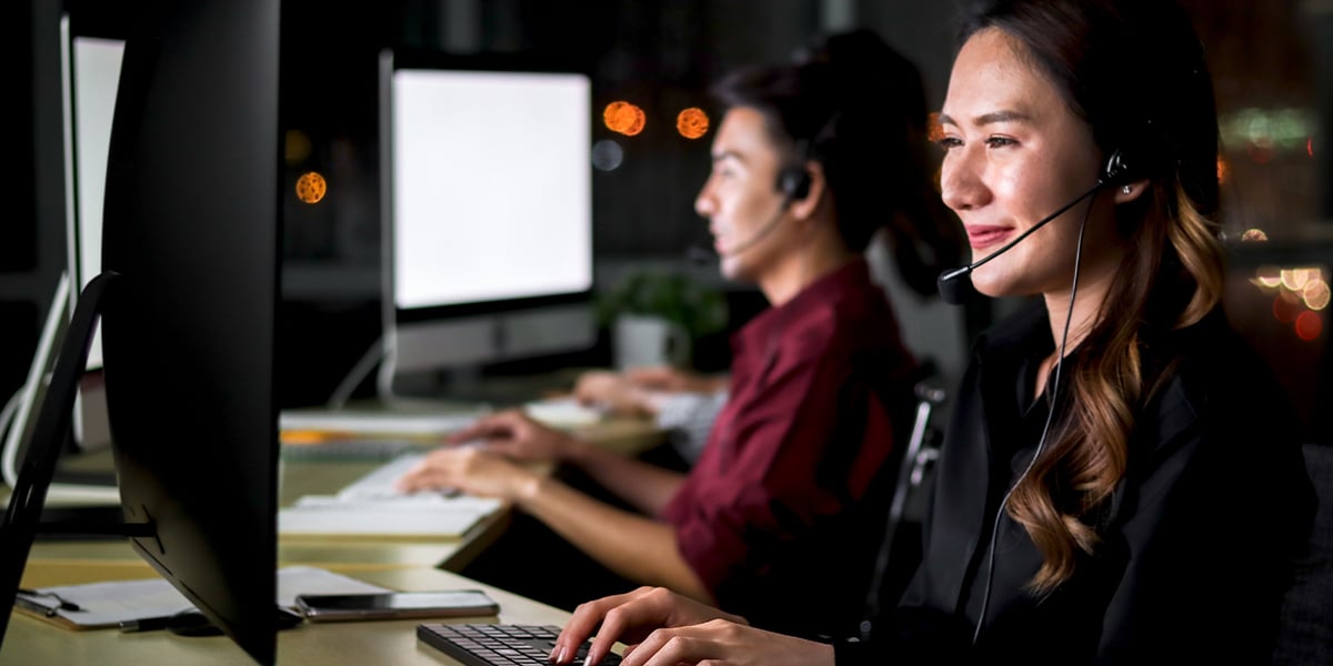 Two customer support people sitting at their desks with headsets on in a call center