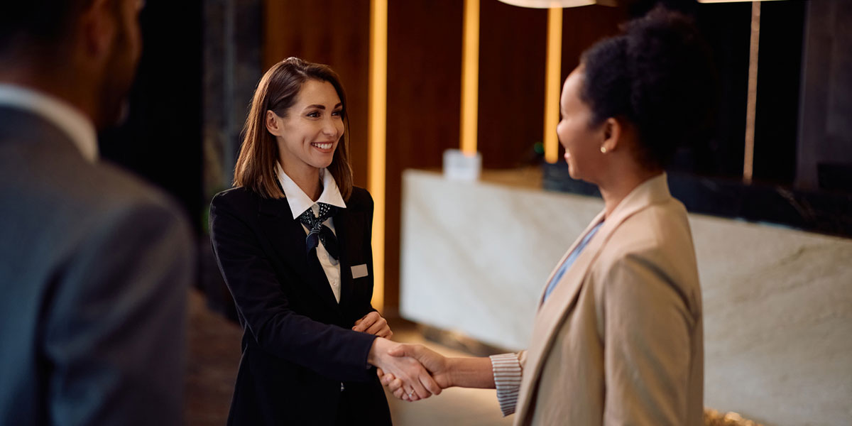 Happy female concierge greeting a business couple in hotel lobby.